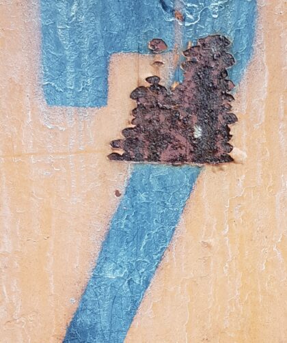Rostige Stahlplatte mit markanter Rostmarke und blauer Zahl 7 auf orange-gelbem Untergrund. Fotodruck auf Dibond oder Forex in diversen Formaten.